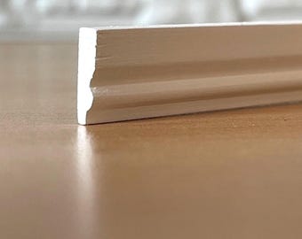 May include: A white painted wooden molding strip with a smooth, matte finish. The piece features a linear profile with a single horizontal groove running along its length, showcasing a clean, rectangular cross-section at the cut end.