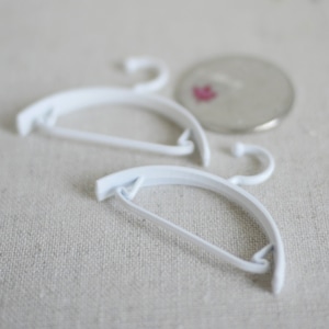 May include: Two white plastic hangers, one on top of the other, with a hook on each end.