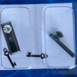 May include: Two black metal door knobs with keys. One knob has a clear rhinestone.