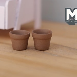 May include: Two small brown terracotta flower pots on a wooden surface. The pots are approximately 5 cm in diameter.