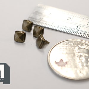 May include: Four small, square, antique gold-coloured metal studs with a raised pyramid design. The studs are approximately 1.25 cm in diameter and are shown next to a ruler and a Canadian coin.