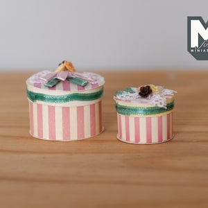 May include: Two round, pink and white striped boxes with green ribbon and floral embellishments. The boxes are made for miniatures.