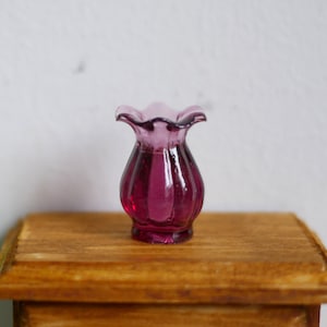 May include: A small, purple glass vase with a ruffled top. The vase is sitting on a wooden surface.