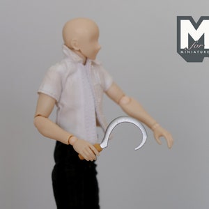 May include: A silver-colored metal hook with a wooden handle. The hook is curved and has a sharp point. The hook is held by a person wearing a white shirt and black pants.