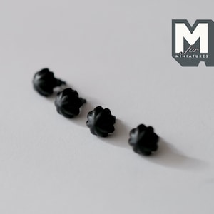 May include: Four black plastic flower-shaped embellishments, possibly for use in miniature crafts or dollhouse decor.
