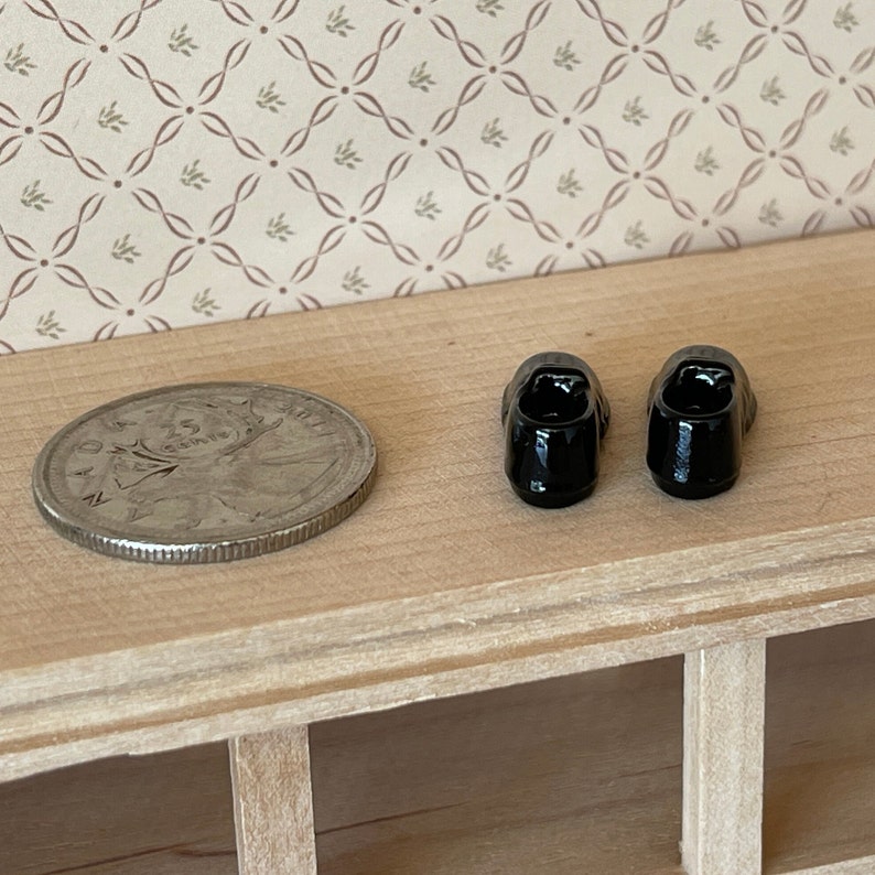 Pu&ograve; includere: Un paio di scarpe nere in miniatura, mostrate accanto a una moneta canadese da 25 centesimi per la scala.