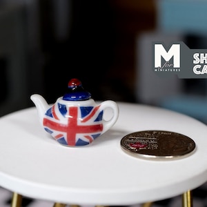 May include: A miniature white teapot with a red, white, and blue Union Jack design. The teapot has a small, blue lid with a red knob.