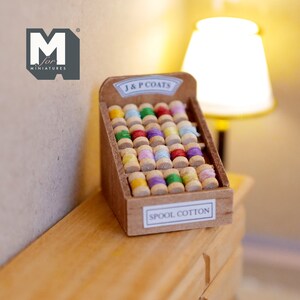 Op de afbeelding: Een miniatuur houten spoel katoen display met de tekst "J & P COATS" en "SPOOL COTTON". Het display is gevuld met kleurrijke spoelen garen.