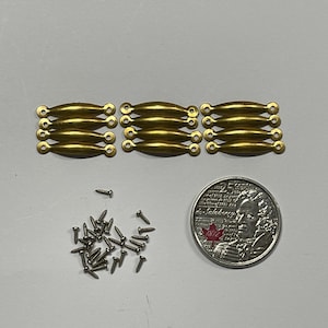 May include: A set of 12 gold-toned metal drawer pulls with a rounded rectangular shape. The pulls are arranged in three rows of four. A pile of small silver screws is also included.