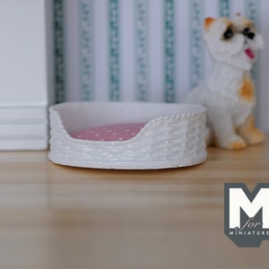 May include: White wicker dog bed with a pink polka dot cushion. The bed is on a wooden surface with a white wall and green and white striped wallpaper in the background. The text "M for Miniatures" is visible in the lower right corner of the image.