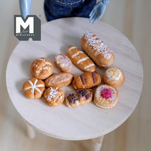 May include: A collection of miniature baked goods, including bread, rolls, and pastries, arranged on a wooden surface. The baked goods are all different shapes and sizes, and some are decorated with icing or sprinkles.