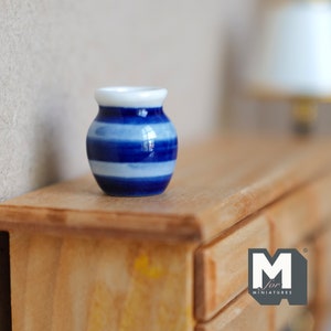 May include: A miniature blue and white striped ceramic vase. The small vase has a rounded body and a white rim. The blue stripes are horizontal and vary in shade. The vase is displayed on a wooden surface.