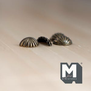 May include: Four antique gold-toned metal shell-shaped embellishments. These decorative accents are perfect for adding a touch of vintage charm to craft projects.