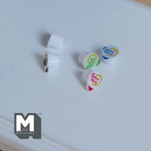 May include: Miniature coffee creamer pods in white with colorful labels. The labels read "Coffee mate" in various colors, including red, green, and blue. The pods are arranged on a white surface, perfect for dollhouses or miniature displays.