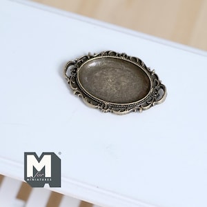 May include: An antique-style, oval-shaped metal tray with ornate filigree edging. The tray has a tarnished, bronze-like finish and is set against a white surface. The tray is likely for miniatures.