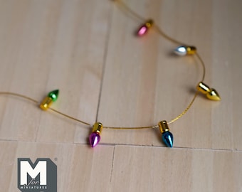 May include: A string of miniature Christmas lights with green, pink, blue, and silver bulbs. The lights are strung on a gold wire and are hanging on a wooden surface.