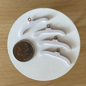 Op de afbeelding: Vier witte houten hangers met gouden metalen haken. De hangers zijn gestapeld op een wit oppervlak.