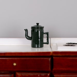 May include: A dark green enamel teapot with a lid and a handle. The teapot is sitting on a white countertop.