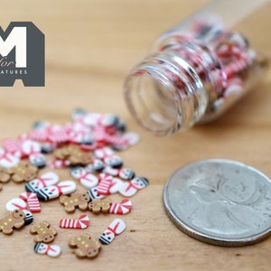 May include: A small glass jar filled with miniature gingerbread men, candy canes, and snowmen. The jar is tipped over, spilling the miniature Christmas decorations onto a wooden surface.