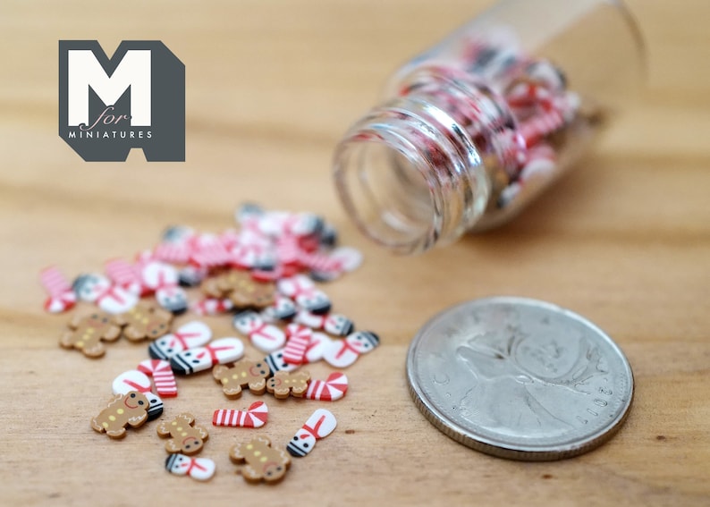 May include: A small glass jar filled with miniature gingerbread men, candy canes, and snowmen. The jar is tipped over, spilling the miniature Christmas decorations onto a wooden surface.