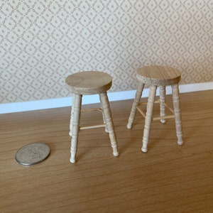 May include: Two wooden stools with a simple design. The stools are made of light brown wood and have a round seat and four legs.