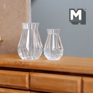 May include: Two clear glass vases with a diamond pattern. The larger vase is taller and has a wider base. The smaller vase is shorter and has a narrower base. Both vases are sitting on a wooden surface.
