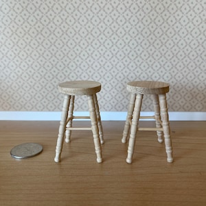 May include: Two wooden stools with a simple design, each with four legs and a single crossbar for support. The stools are made of light brown wood and are sitting on a wooden floor.