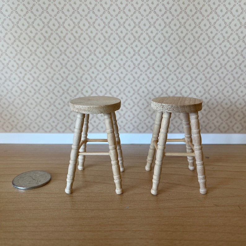 May include: Two wooden stools with a simple design, each with four legs and a single crossbar for support. The stools are made of light brown wood and are sitting on a wooden floor.