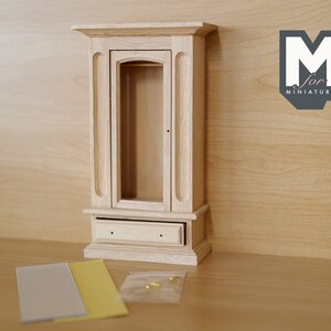 May include: A wooden dollhouse cabinet with a glass door and a drawer. The cabinet is unfinished and ready to be painted or stained.