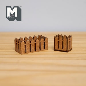 May include: Two miniature wooden picket fences. One is rectangular, the other is square. Both are made of light brown wood and have pointed tops. The fences are designed for use in a miniature scene or diorama.