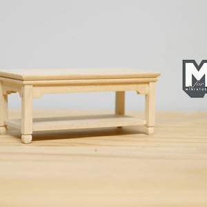 May include: Unpainted wooden coffee table with a shelf, featuring a simple design with rounded legs. The table is approximately 12 inches long and 6 inches wide.