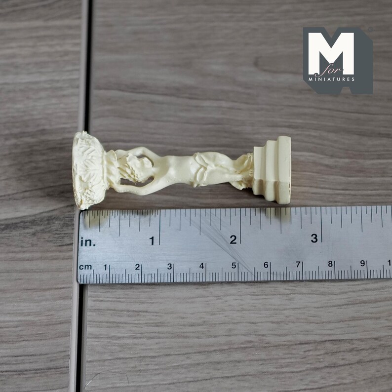 Puede incluir: Una estatua de cer&aacute;mica blanca de una mujer sosteniendo un jarr&oacute;n, de pie sobre un pedestal. La estatua mide aproximadamente 5 cm de alto.