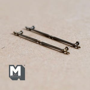 May include: Two antique bronze-colored miniature door handles. Each handle has a long, slender bar with decorative ends. The handles are designed for dollhouses or other miniature projects. The logo "M for miniatures" is in the lower left corner.