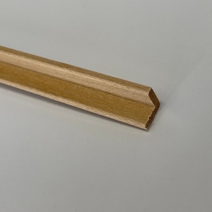 May include: A close-up of a light brown wooden trim piece with a beveled edge. The trim has a subtle groove running along its length.