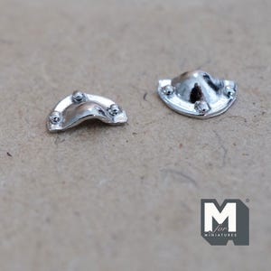 May include: Two small, shiny silver metal drawer pulls for miniature furniture. One is curved with three small ball accents, and the other is a rounded shape with three ball accents. The pulls are on a neutral background.