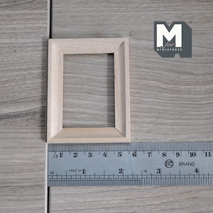 May include: A small, unfinished wooden rectangular frame, likely for miniatures. A metal ruler with inch and centimetre markings is placed next to the frame. The frame is approximately 5 cm wide. The logo "M for MINIATURES" is visible.