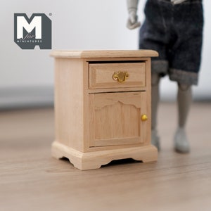 Peut inclure: Une table de chevet miniature en bois avec un tiroir et une porte. Le tiroir a une poign&eacute;e dor&eacute;e et la porte a un bouton dor&eacute;. La table de chevet est en bois clair et a un design simple.