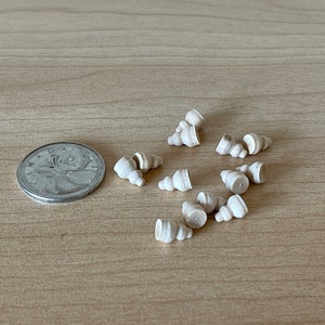 May include: A collection of small, white, wooden seashells on a light brown wooden surface.