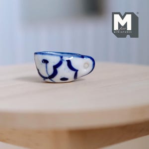 May include: A small white ceramic teacup with a blue floral design and a handle. The cup is sitting on a wooden surface.