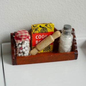 May include: A wooden shelf with a red and white gingham jar filled with white beads, a yellow cookbook with the text "COOK BOOK", a wooden rolling pin, and a clear glass jar with a grey lid filled with white crystals.