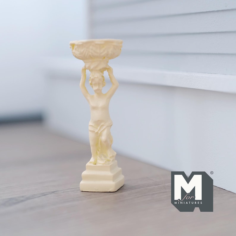 Puede incluir: Una estatua de cer&aacute;mica blanca de una figura que sostiene una maceta en la cabeza. La estatua est&aacute; sobre un pedestal y tiene un dise&ntilde;o detallado.