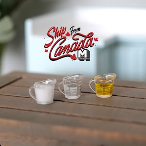 May include: Three miniature measuring cups, one filled with white liquid, one with clear liquid, and one with yellow liquid. The cups are on a wooden surface.