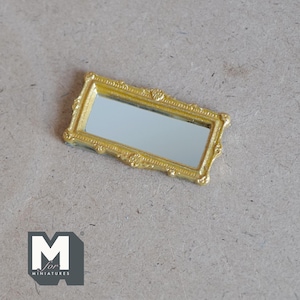 May include: A gold-colored rectangular mirror with an ornate frame. The mirror is small and would be suitable for a dollhouse or miniature setting.