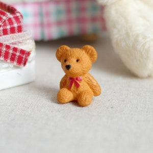 May include: A small brown teddy bear with a red bow sitting on a white surface.