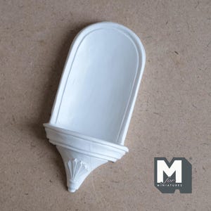 Può includere: Mensola in gesso bianco con parte superiore curva e design decorativo. La mensola è progettata per essere montata a parete.