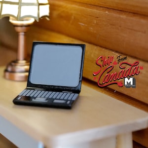May include: A black laptop computer with a blank screen is on a light brown wooden desk. A small lamp with a white shade is on the desk to the left of the laptop. The desk is in front of a wall made of wood planks.