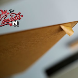May include: A close-up of a brown cardboard box with a piece of tape on the corner. The box is angled upwards and the top of the box is out of focus. The text "Ship from Canada" is visible in the background.