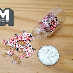May include: A small glass jar filled with miniature gingerbread men and candy canes. The jar is tipped over and the miniature candies are scattered on a wooden surface.