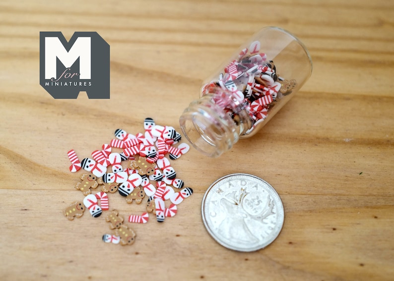 May include: A small glass jar filled with miniature gingerbread men and candy canes. The jar is tipped over and the miniature candies are scattered on a wooden surface.