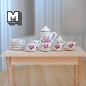 May include: A miniature tea set featuring a white teapot, sugar bowl, creamer, and four cups and saucers. The set is decorated with pink roses and green leaves. The set is displayed on a wooden table.